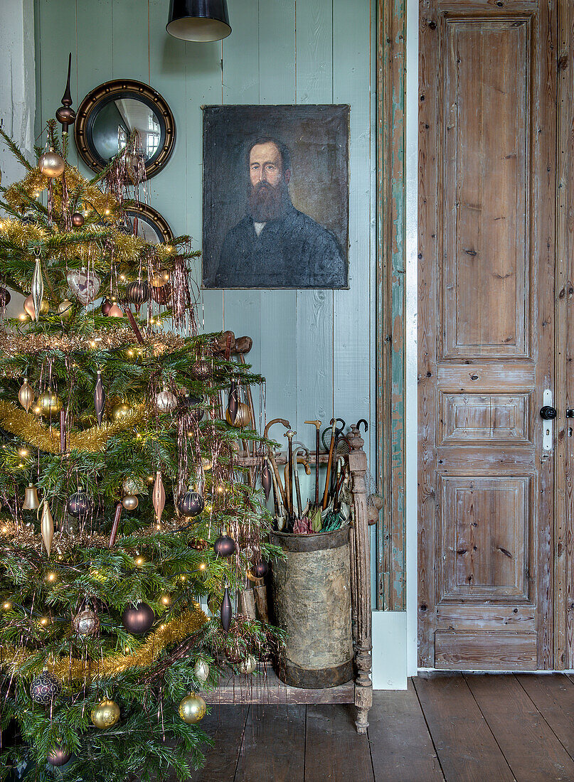 Weihnachtlich geschmückter Flur mit Weihnachtsbaum, antikem Regenschirmständer und Ölgemälde