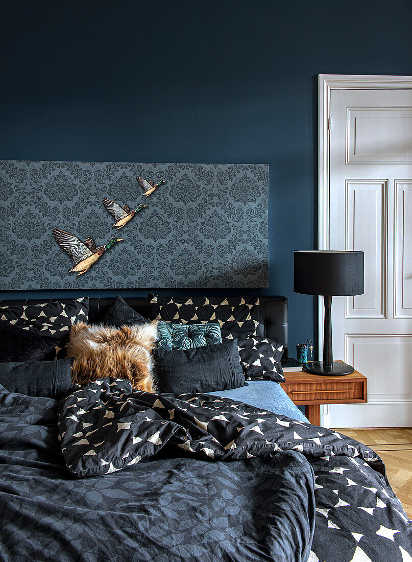 Bedroom with dark blue wall, patterned bed linen and black bedside lamp