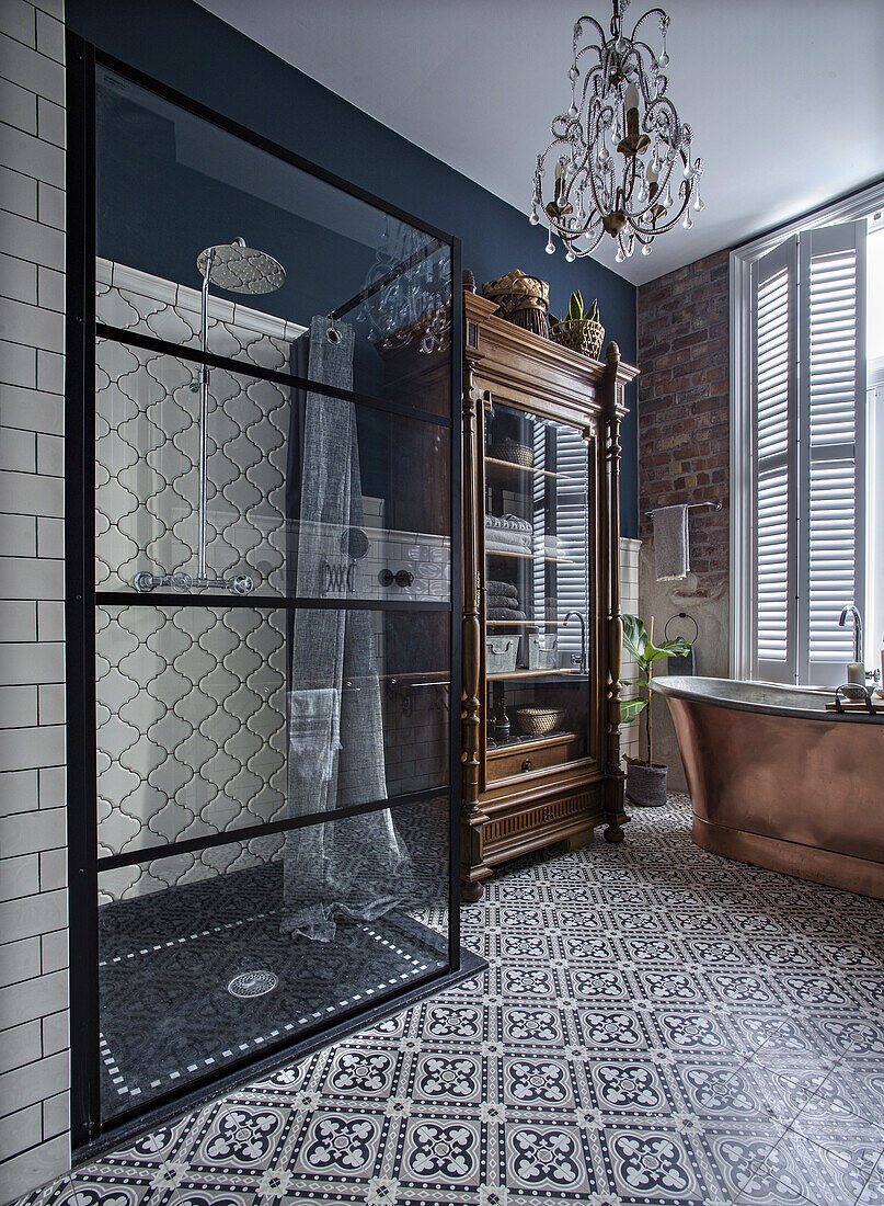 Bathroom with patterned floor tiles, freestanding copper bathtub and antique display cabinet