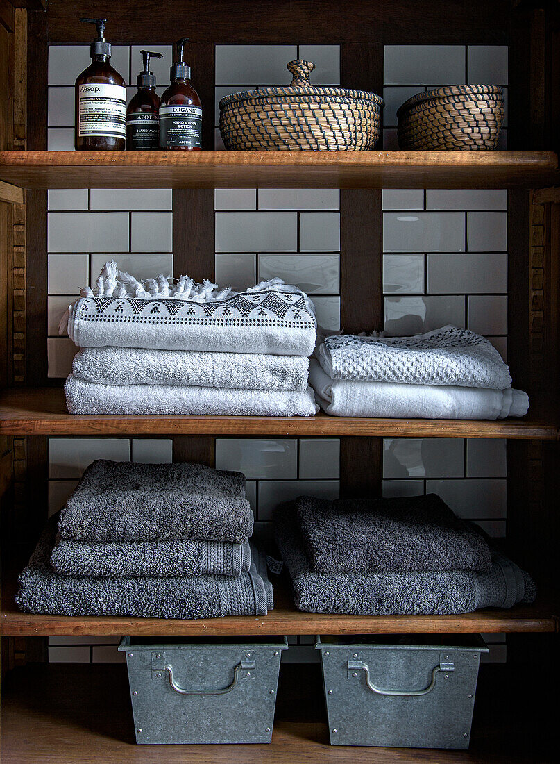 Shelves with folded towels, baskets and metal boxes in front of white tiled wall