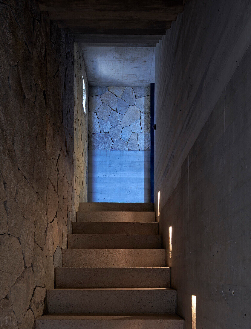 View from bottom of an illuminated concrete staircase between stone and concrete walls