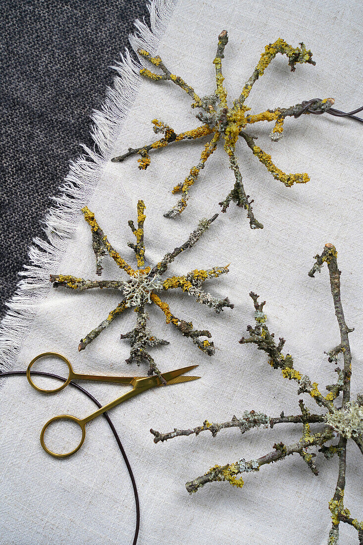 Lichen-decorated stars made from twigs and gold-coloured scissors on white linen fabric