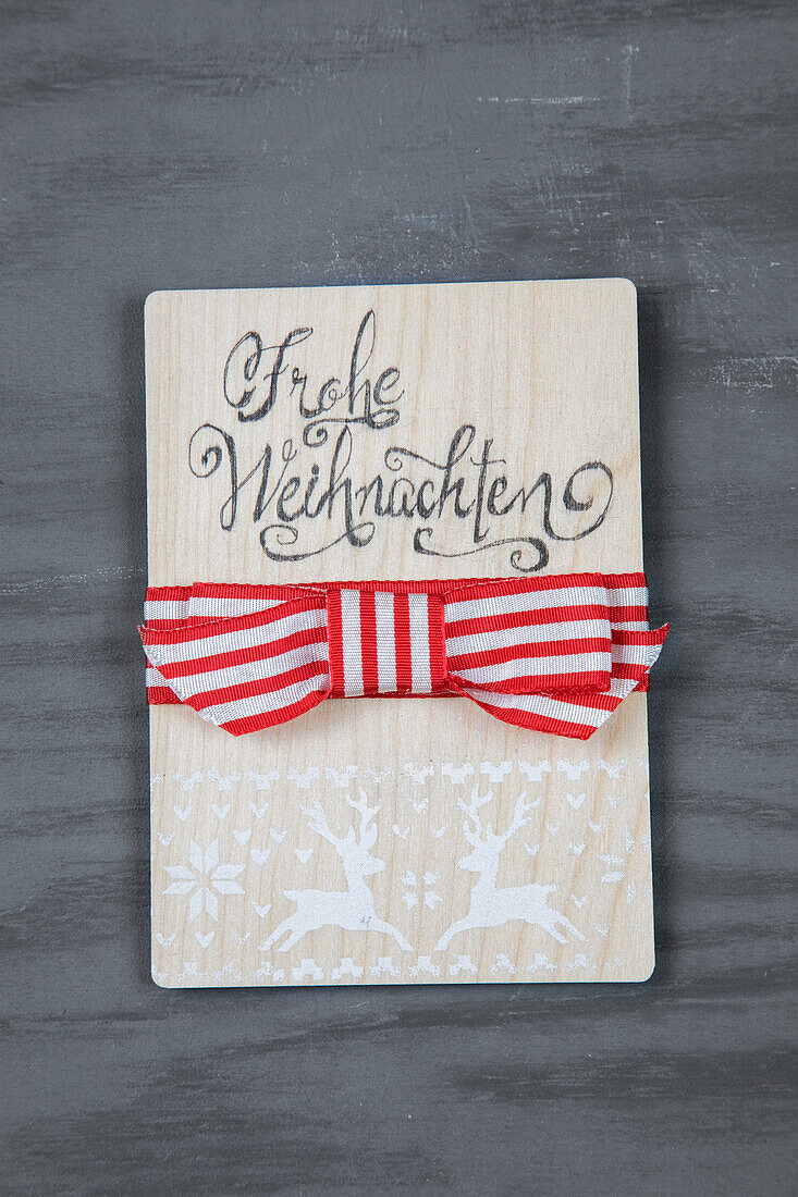 Holzschild mit Schriftzug "Frohe Weihnachten" und rot-weißer Schleife