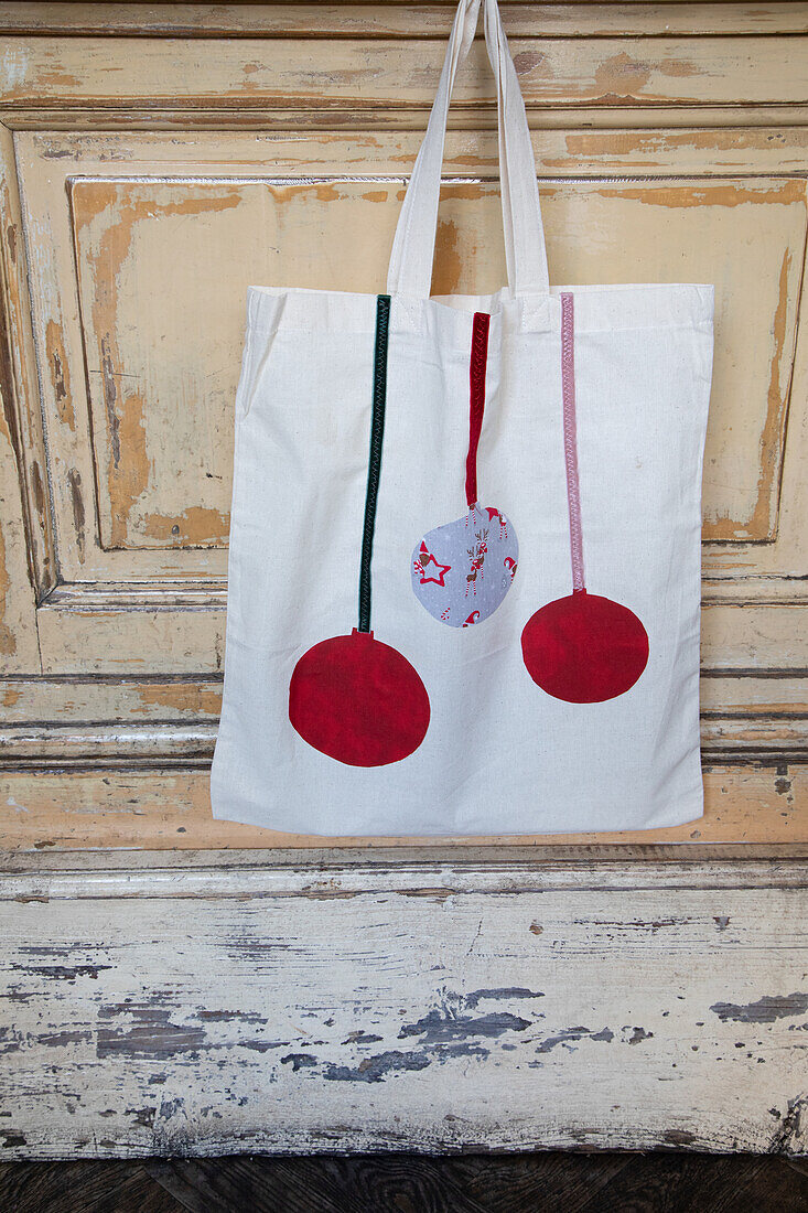 Fabric bag with red Christmas ornament motifs in front of an antique wooden wall