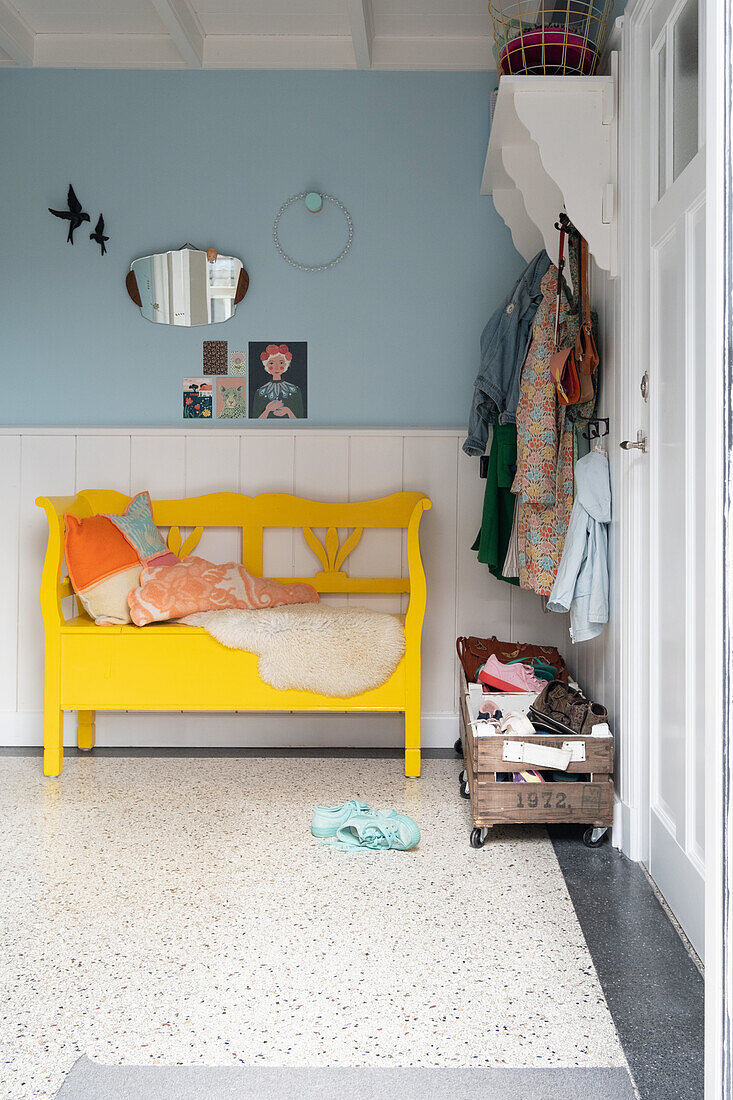 Yellow wooden bench with cushions in the hallway with blue wall and decoration