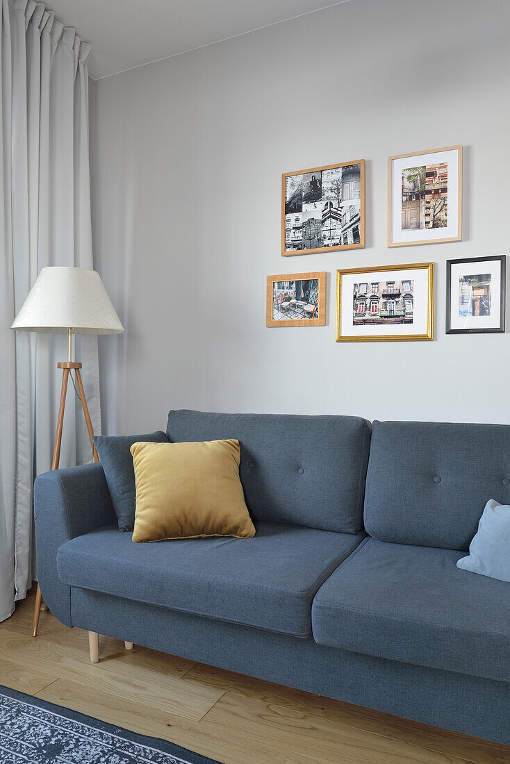 Blue sofa with yellow throw pillow, floor lamp and pictures on the wall