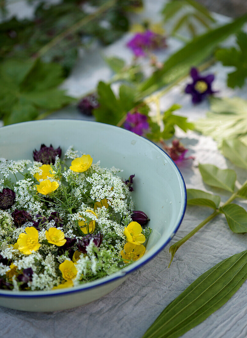 Bowl with wildflowers and herbs on white cloth