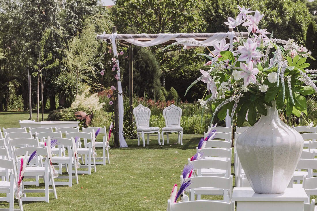 Outdoor wedding area with white chairs and floral decorations in the garden