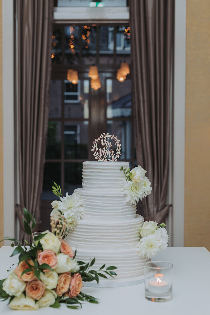 Hochzeitstorte mit weißen Dahlien und Rosen auf festlich gedecktem Tisch