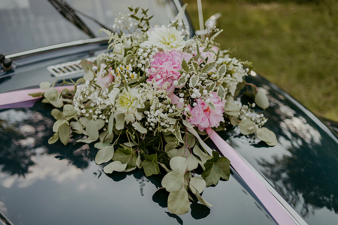 Blumenarrangement aus Eukalyptuszweigen und Pfingstrosen auf Oldtimerhaube