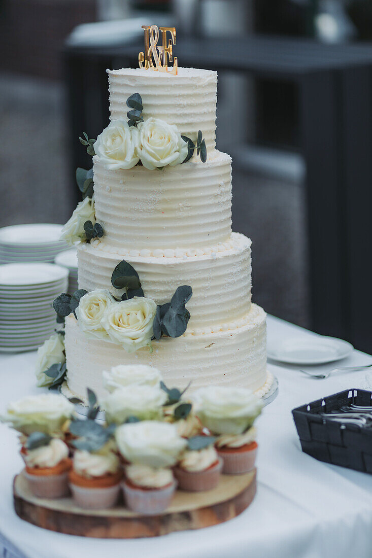 Wedding cake with rose decoration and cupcakes on wooden board