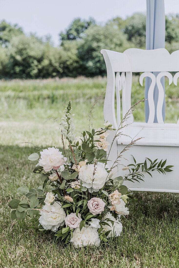 Flower arrangement with peonies and roses in front of white vintage bench in summer