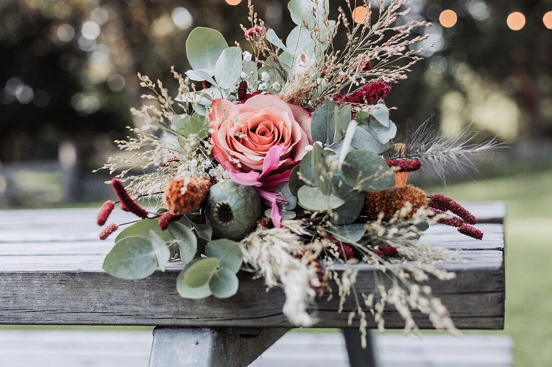 Herbstlicher Blumenstrauß mit Rosen und Eukalyptuszweigen auf Holztisch