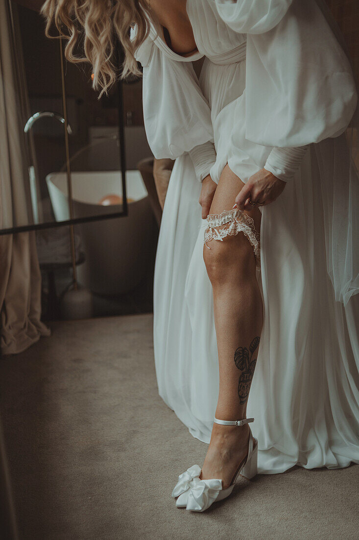 Bride in white dress puts garter on her thigh