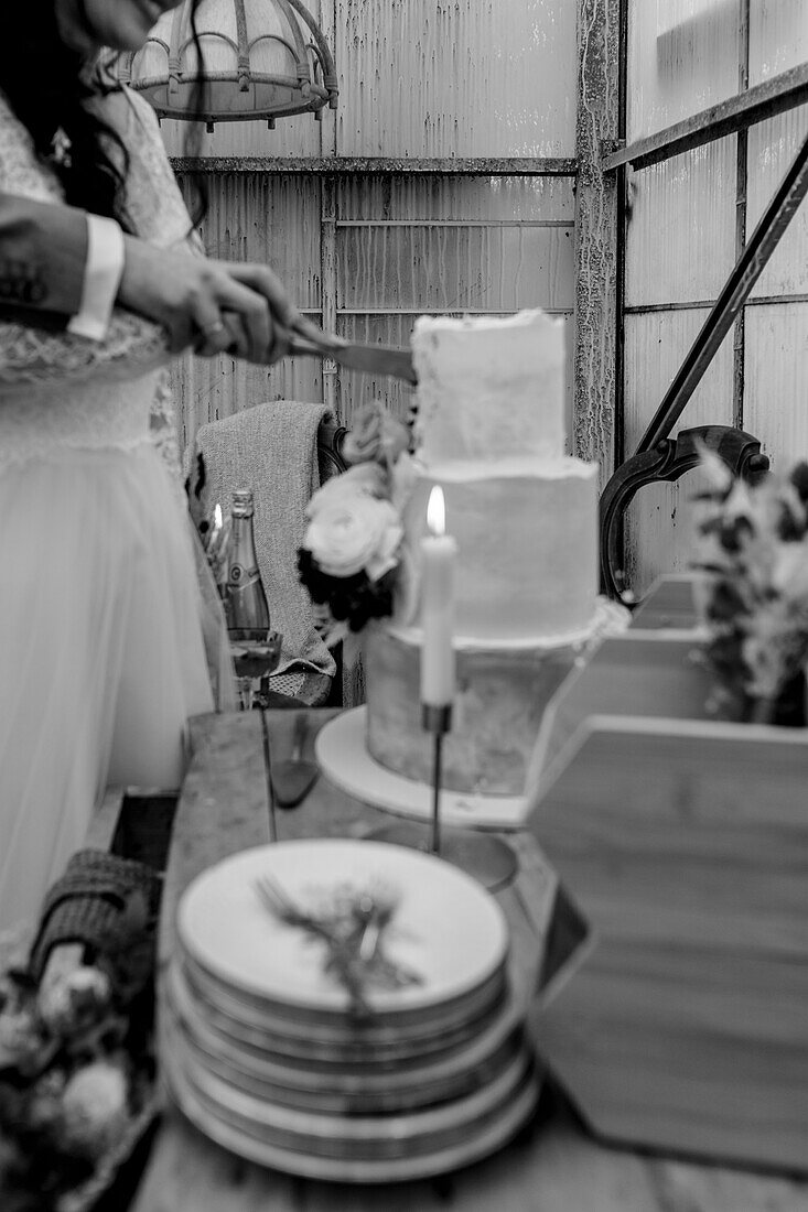 Bridal couple cutting wedding cake, cake plates with forks and candle on table