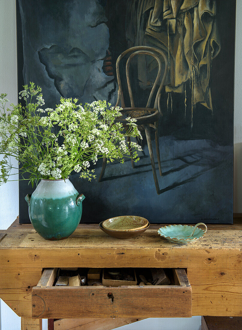 Stillleben mit Gemälde und Keramiktellern, Vase und Blumen auf rustikalem Holztisch