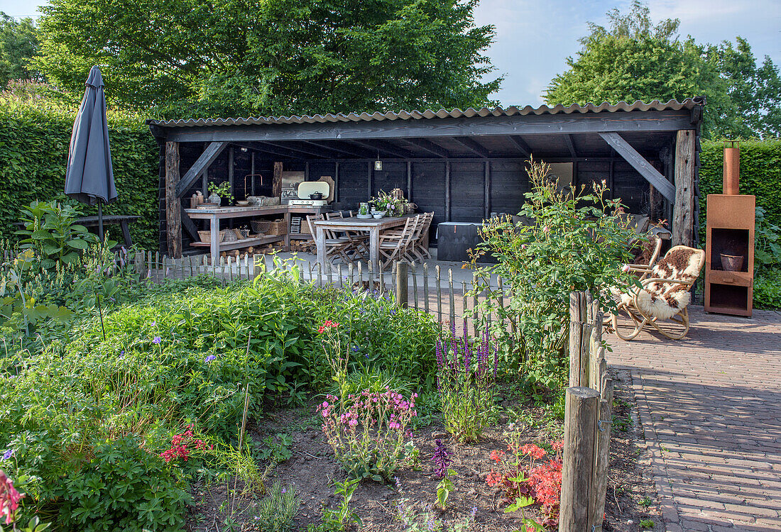 Gazebo with wooden table and chairs, surrounded by flowering shrubs