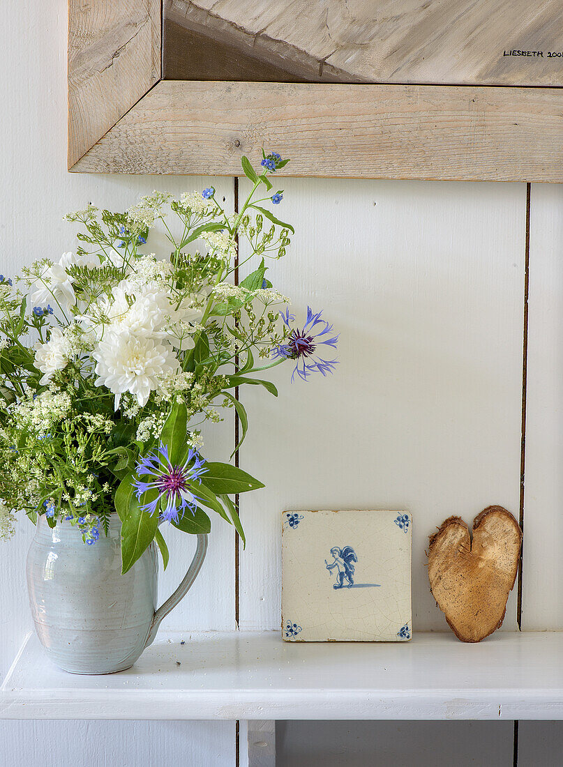 Flower arrangement with white and blue flowers in ceramic vase on wooden shelf