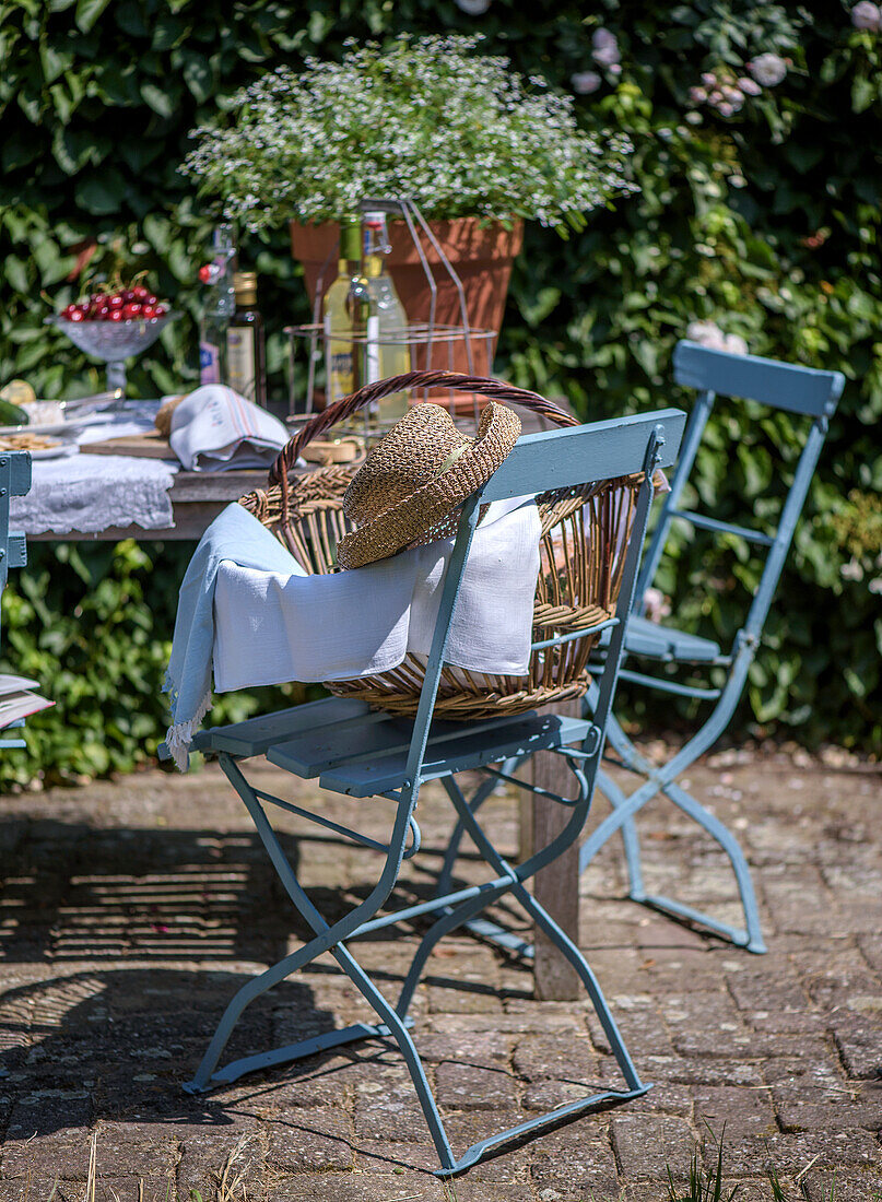 Garten-Sitzbereich mit blauen Stühlen, Strohhut und Weidenkorb