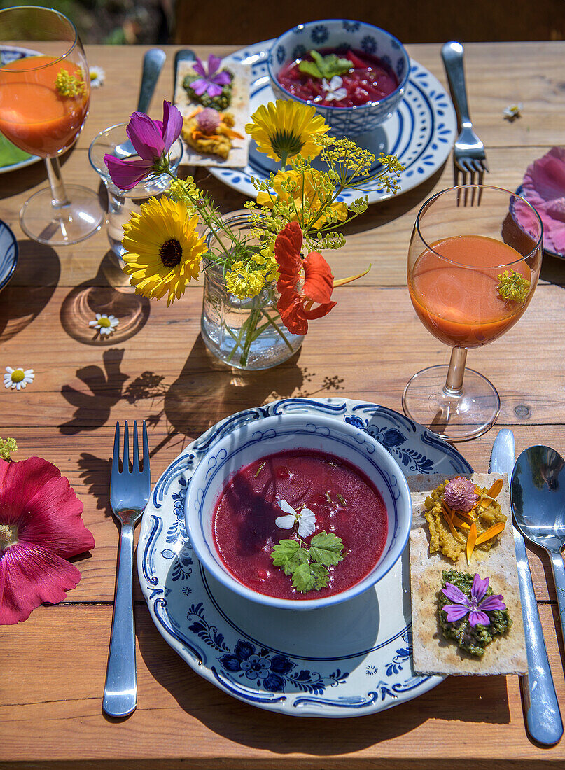 Summery table setting with flower decorations and beetroot soup in bowls