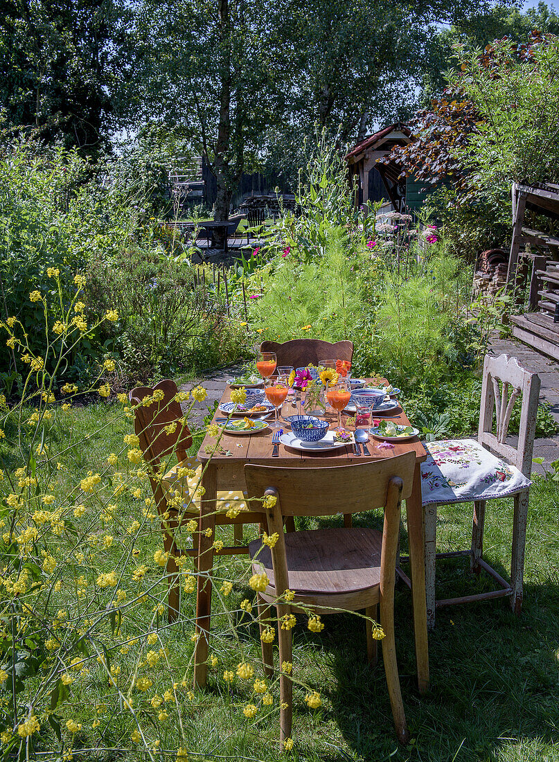 Gedeckter Holztisch im sommerlichen Garten mit Blumen und buntem Geschirr