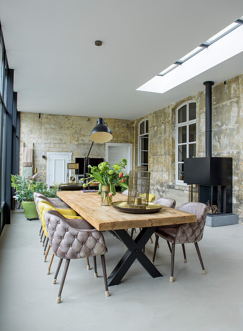 Dining area with long wooden table, upholstered chairs and unplastered walls