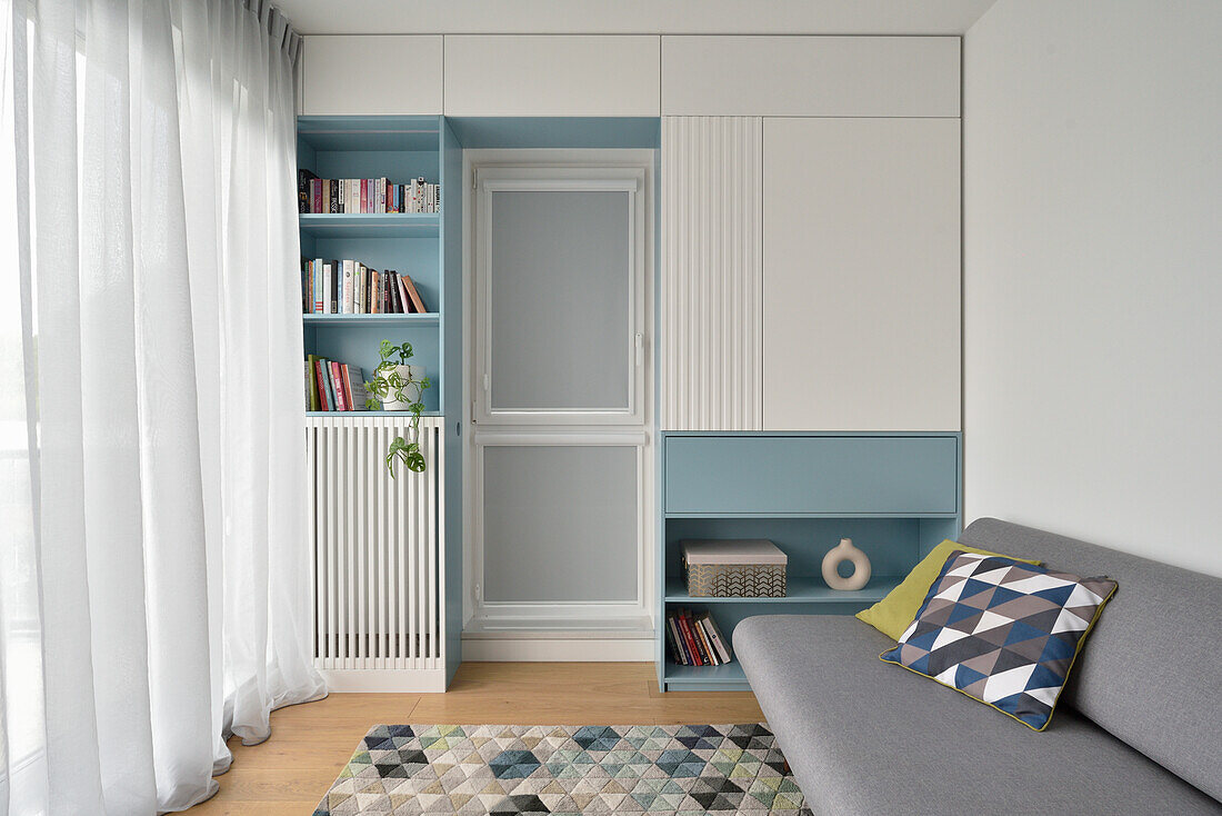 Light blue shelving system in the living room with integrated radiator cover and grey sofa