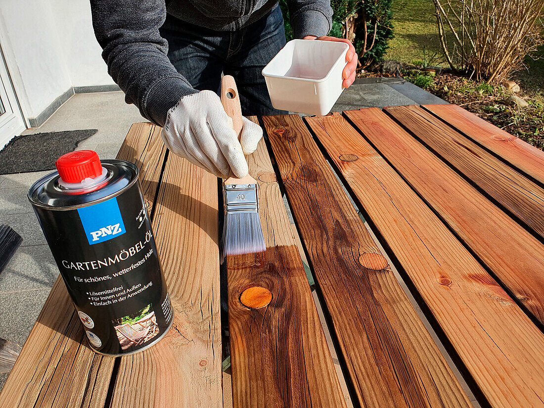 Man treats wooden table with garden furniture oil in the garden