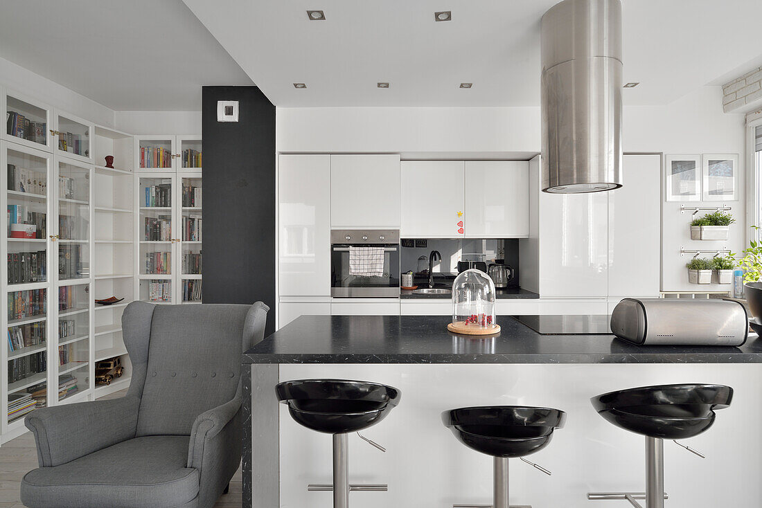 Modern kitchen with bar stools, grey wing chair and built-in bookshelf