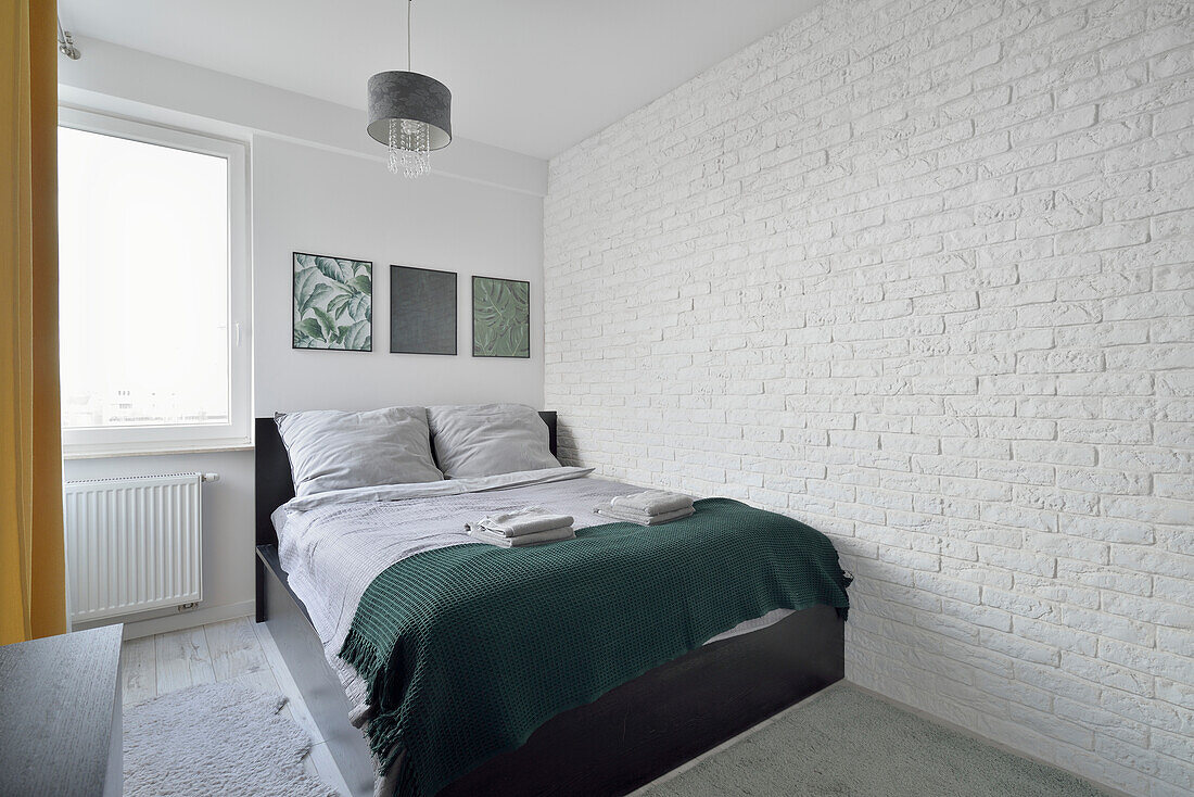 Bedroom with white brick wall and dark green bedspread