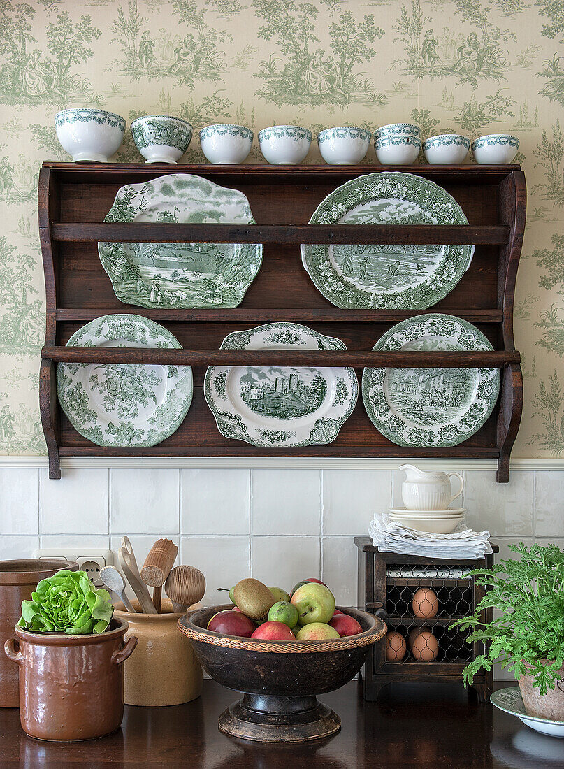 Vintage plate rack with green and white porcelain in front of floral patterned wallpaper