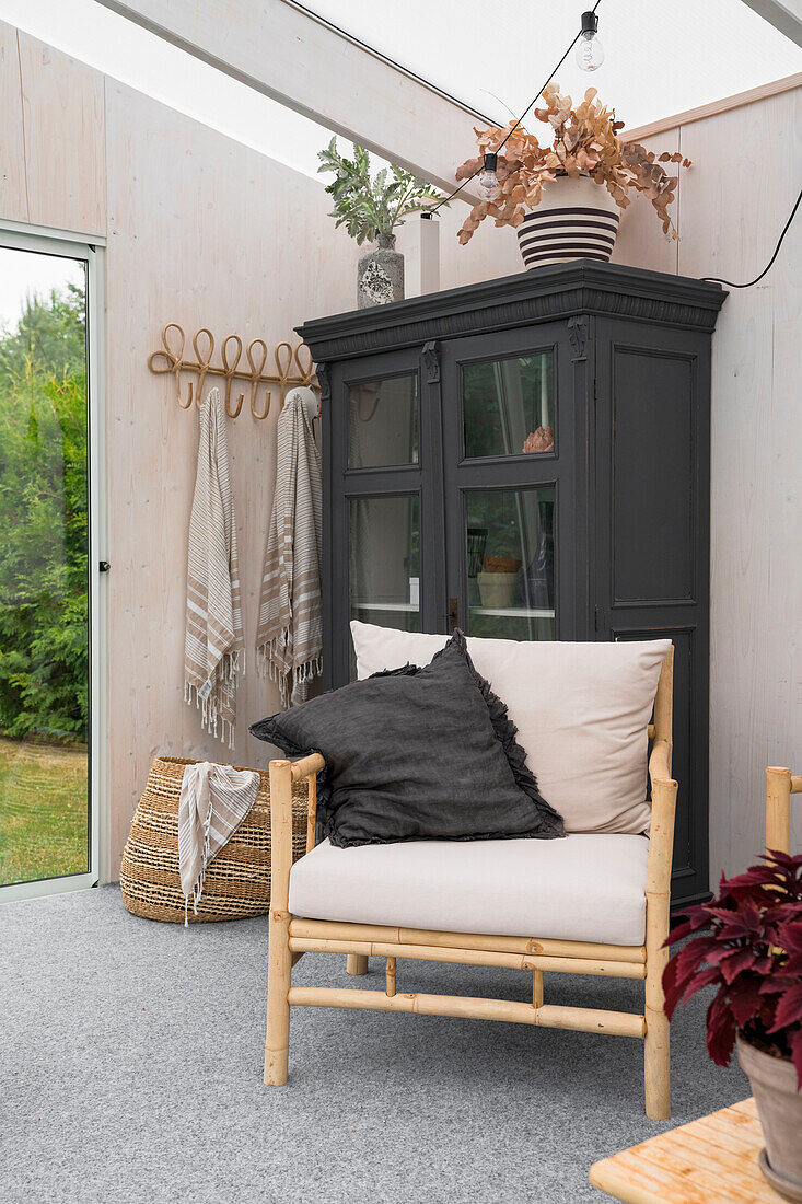 Bamboo armchair in front of black cabinet in light-flooded room with garden view