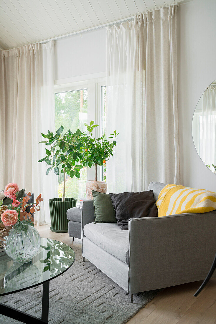 Wohnzimmer mit grauem Sessel, Zimmerpflanzen und rosa Blumenstrauß