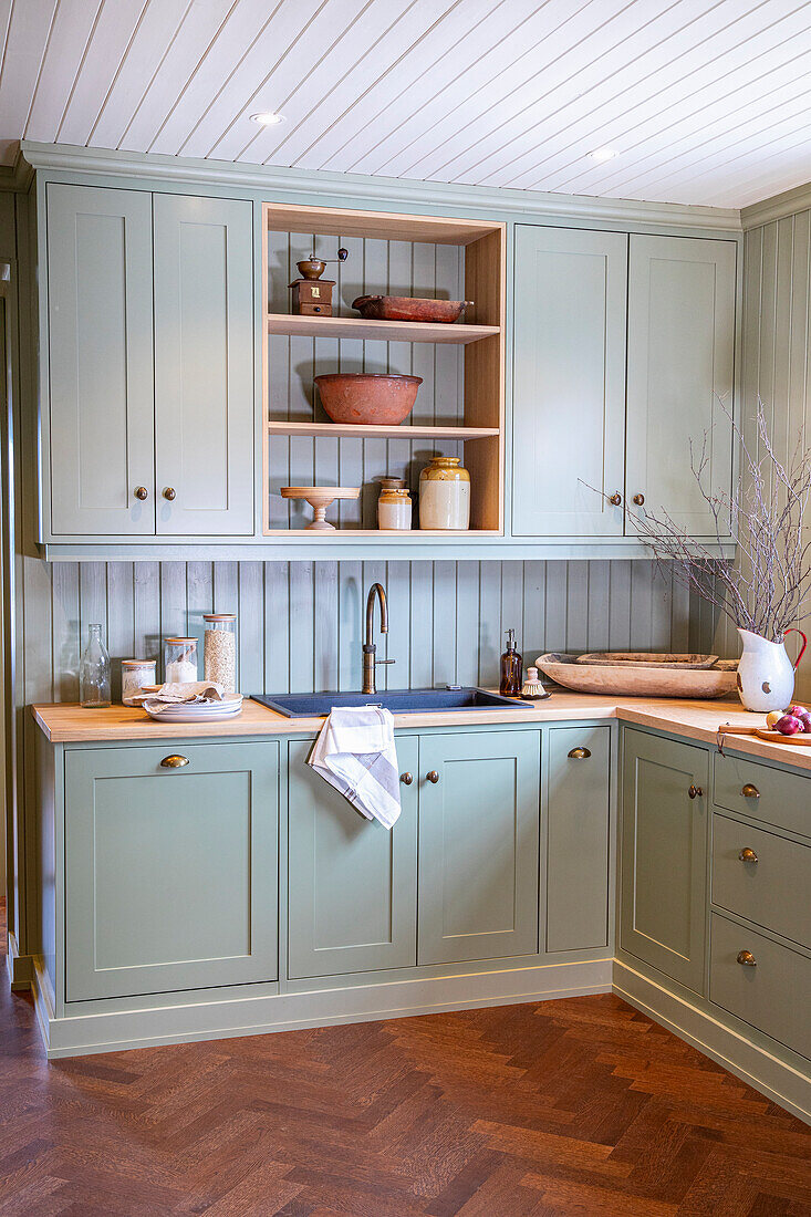 Country-style kitchen with pastel green painted cabinets and wooden worktop