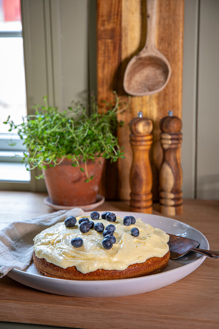 Selbstgebackener Kuchen mit Frischkäse-Topping und Blaubeeren auf rustikaler Küchenanrichte