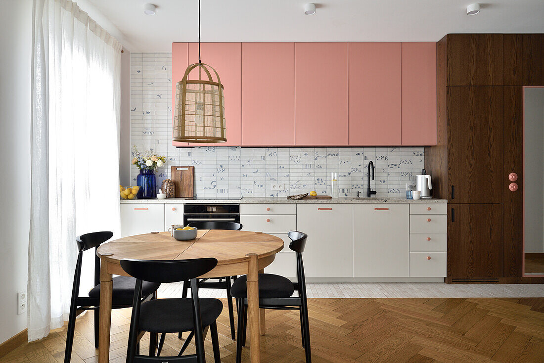 Kitchen with wall units in pink and round wooden table with black chairs