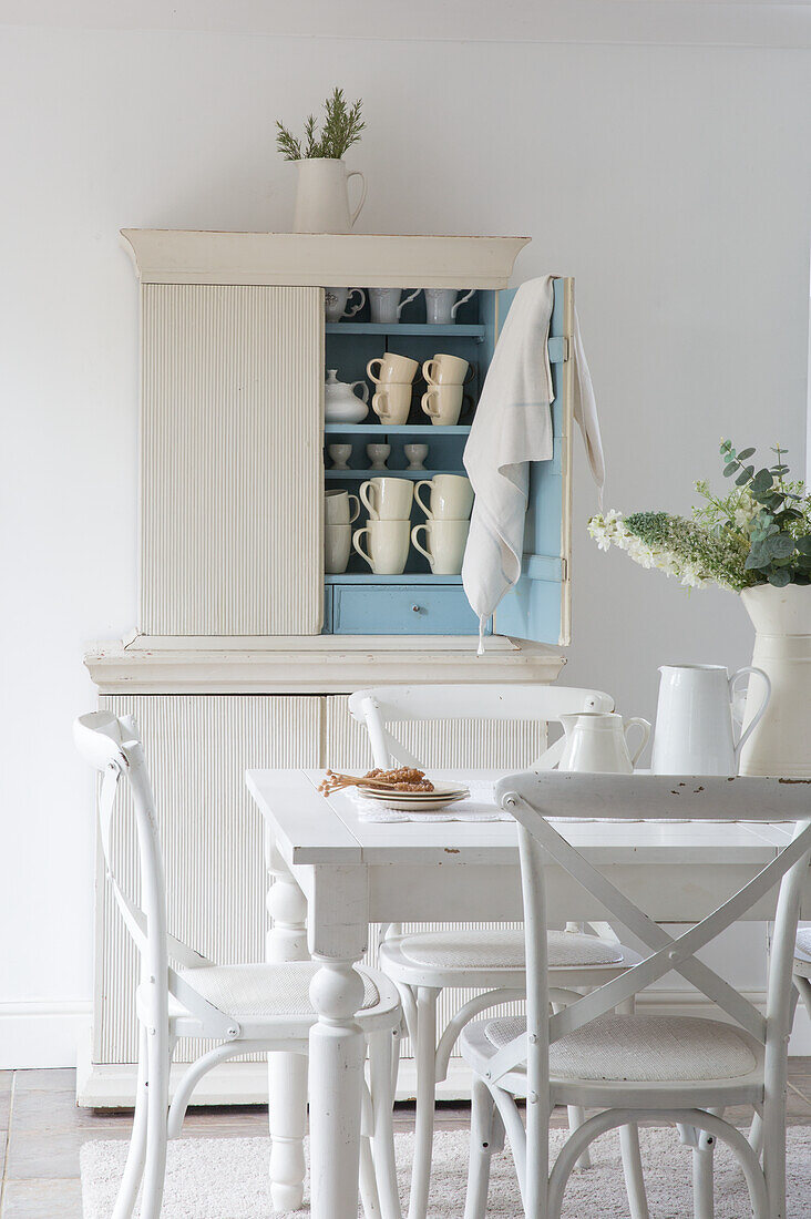 Kitchen cupboard with cups and set dining table with chairs in a shabby chic look