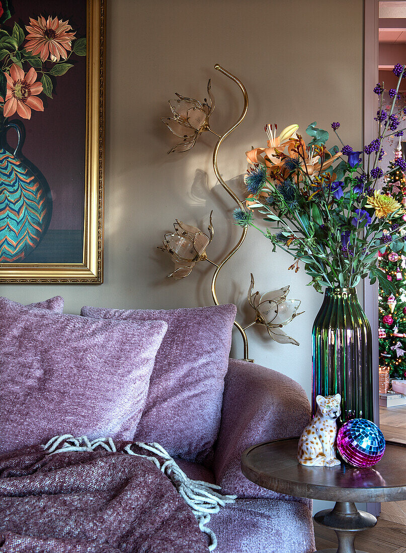 Sofa and cushions in light purple, round wooden table with flower vase next to it