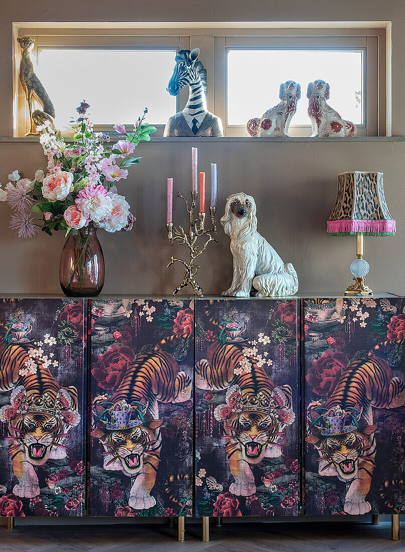 Vase mit Blumen und Kerzenleuchter auf Schrank mit Tiger-Motiv