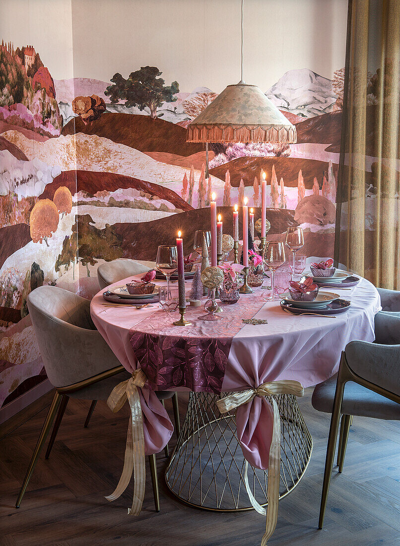 Round dining table with tablecloth, candles and crockery in front of landscape wallpaper