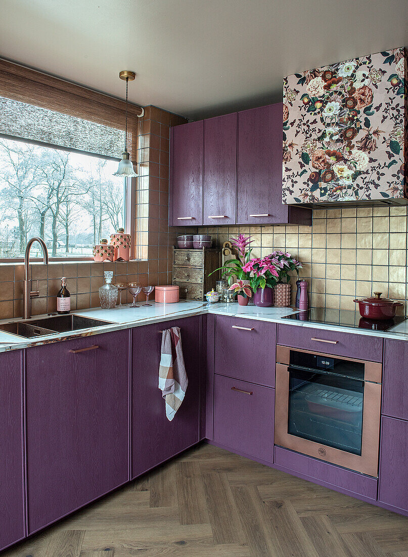 Kitchen with purple cupboards, floral patterned extractor bonnet and herringbone parquet flooring