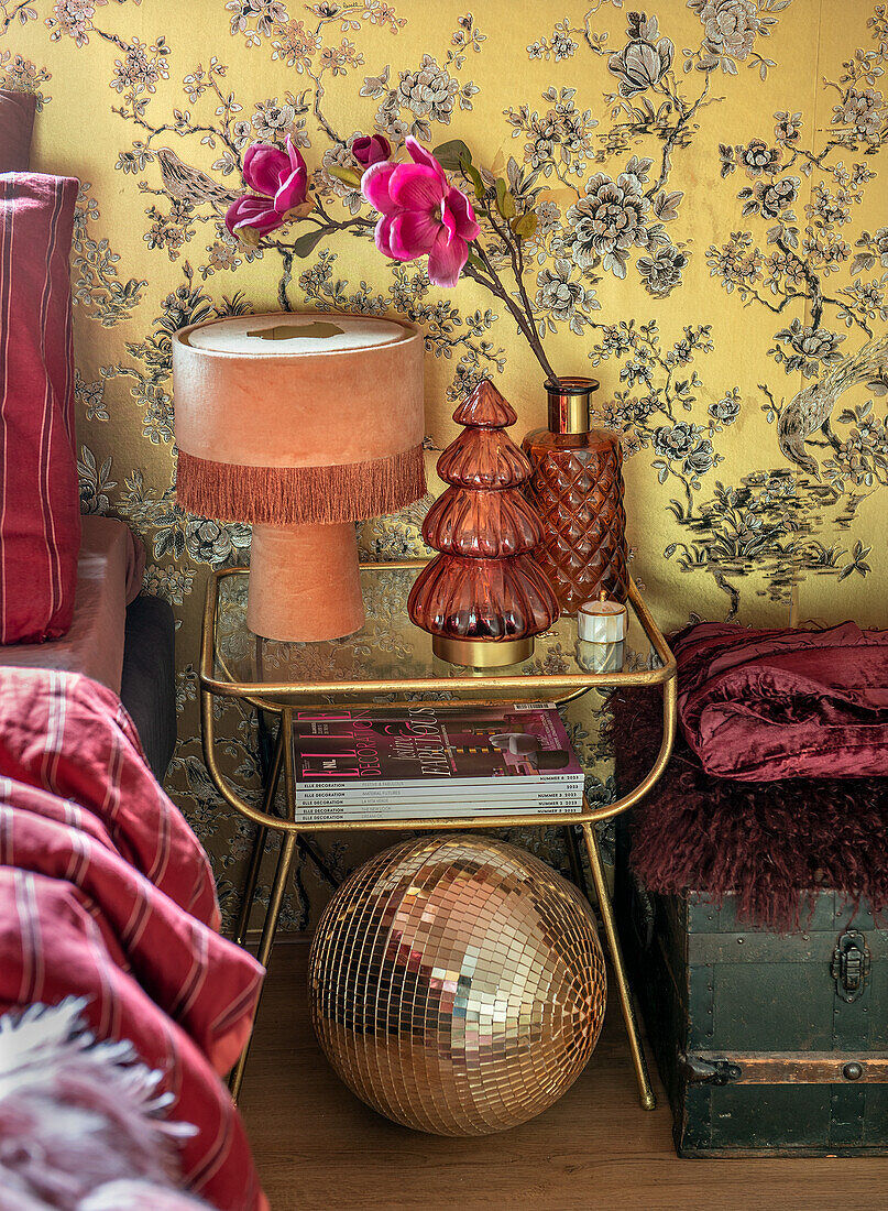 Bedside table with table lamp and decoration in front of yellow wallpaper with floral pattern