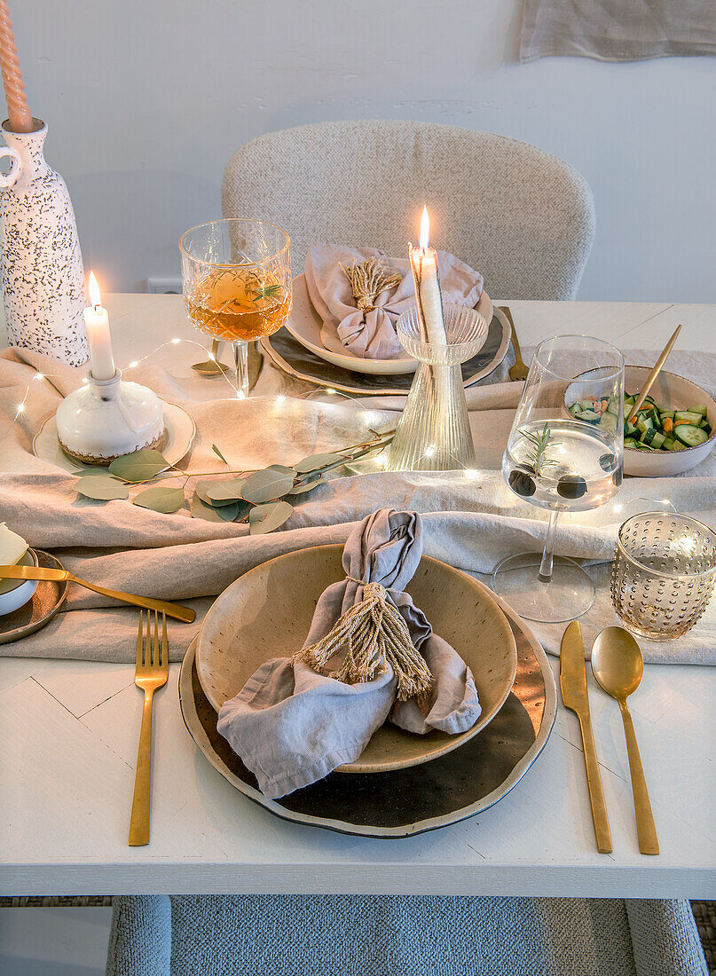 Festively set dining table with gold-coloured cutlery and candlelight