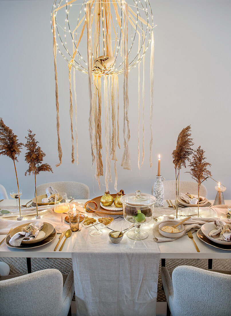 Festively laid dining table with candles and ceiling lamp with fairy lights