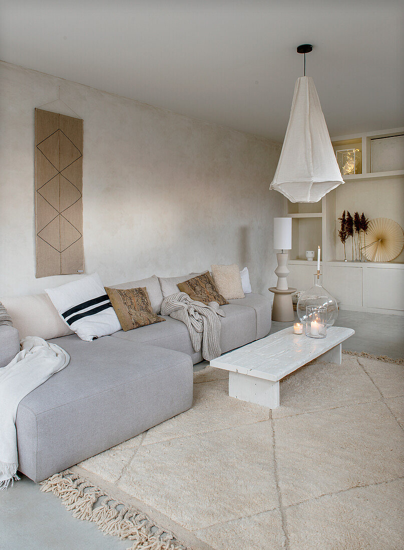 Boho-style living room with grey sofa, beige carpet and white hanging lamp