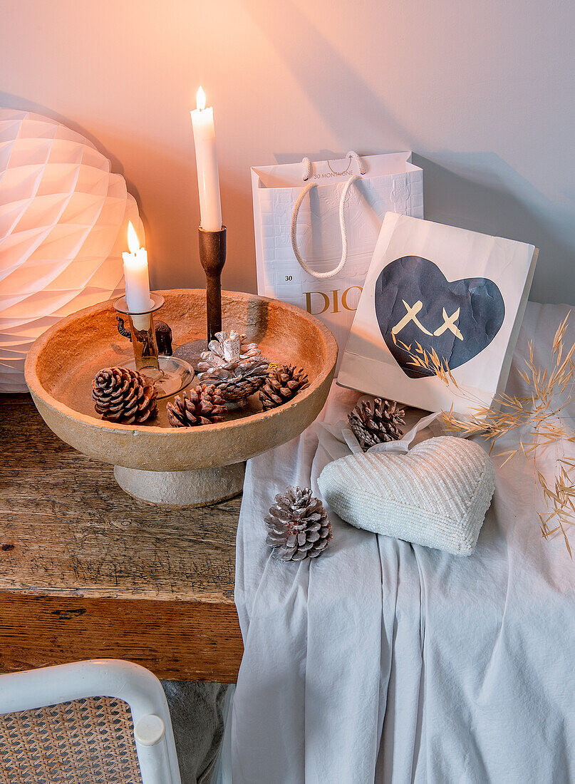 Deko-Arrangement aus Kerzen, Zapfen und Tüten auf Holztisch