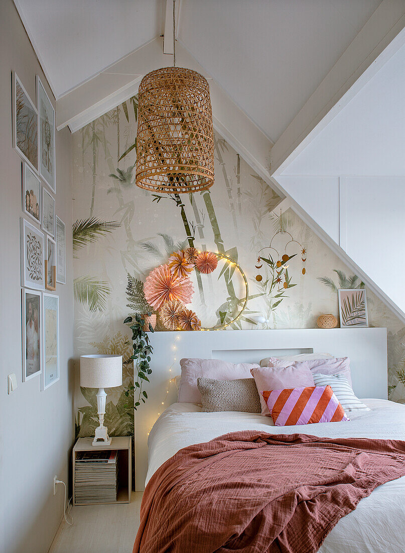 Bedroom with leaf wallpaper, rattan ceiling light and decorative cushions