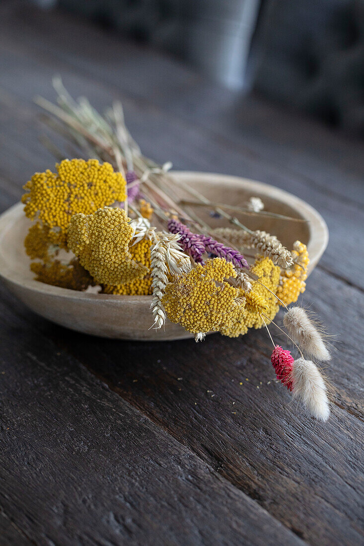 Trockenblumenarrangement in rustikaler Holzschale auf Holztisch