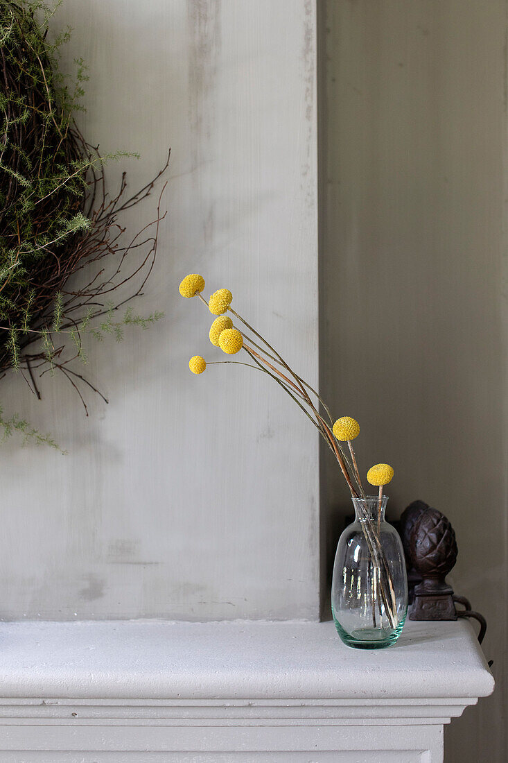 Glass vase with yellow craspedia (drumstick) on a white mantelpiece