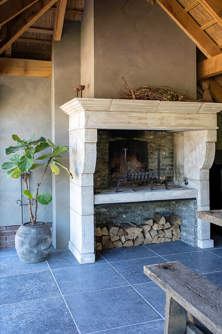 Fireplace with wood storage in covered outdoor area, plant in clay pot